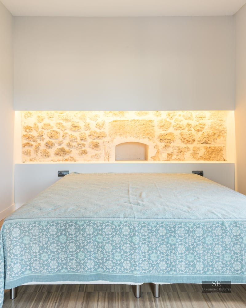 Modern bedroom featuring a bed, an illuminated natural stone wall niche, and light wood flooring.