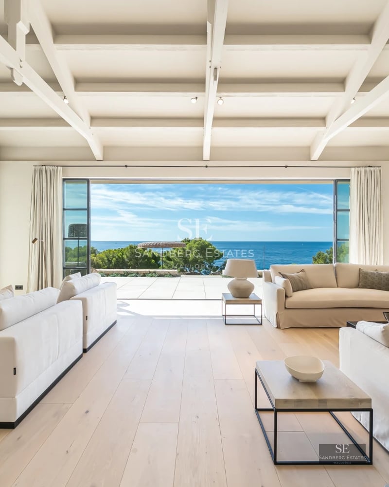 Spacious living room with panoramic windows, light wood floors, modern fireplace, and access to a sea-view terrace. Designer furniture and natural light.