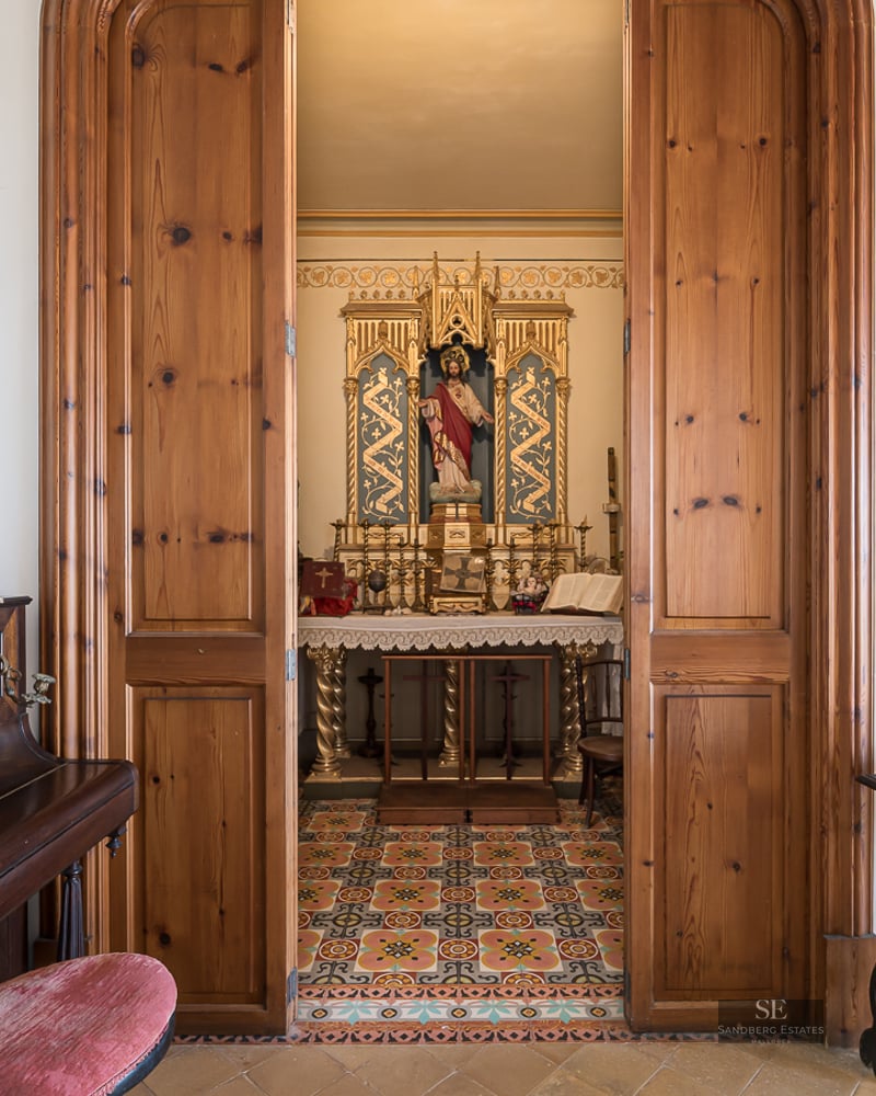 View through wooden doors into a small ornate private chapel with an altar next to an upright piano.