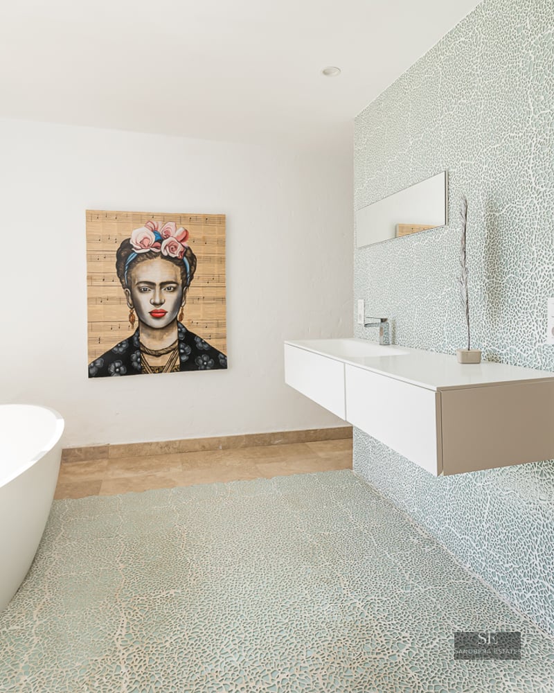 Bright bathroom featuring a white oval tub, floating vanity, blue mosaic wall, and a Frida Kahlo portrait.
