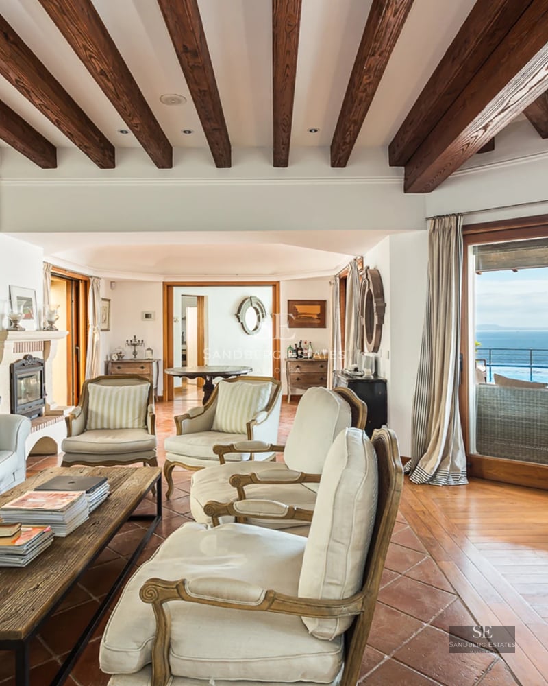 Grand balcon avec vue sur mer depuis un appartement moderne. Garde-corps en verre, plancher en bois et mobilier extérieur élégant.