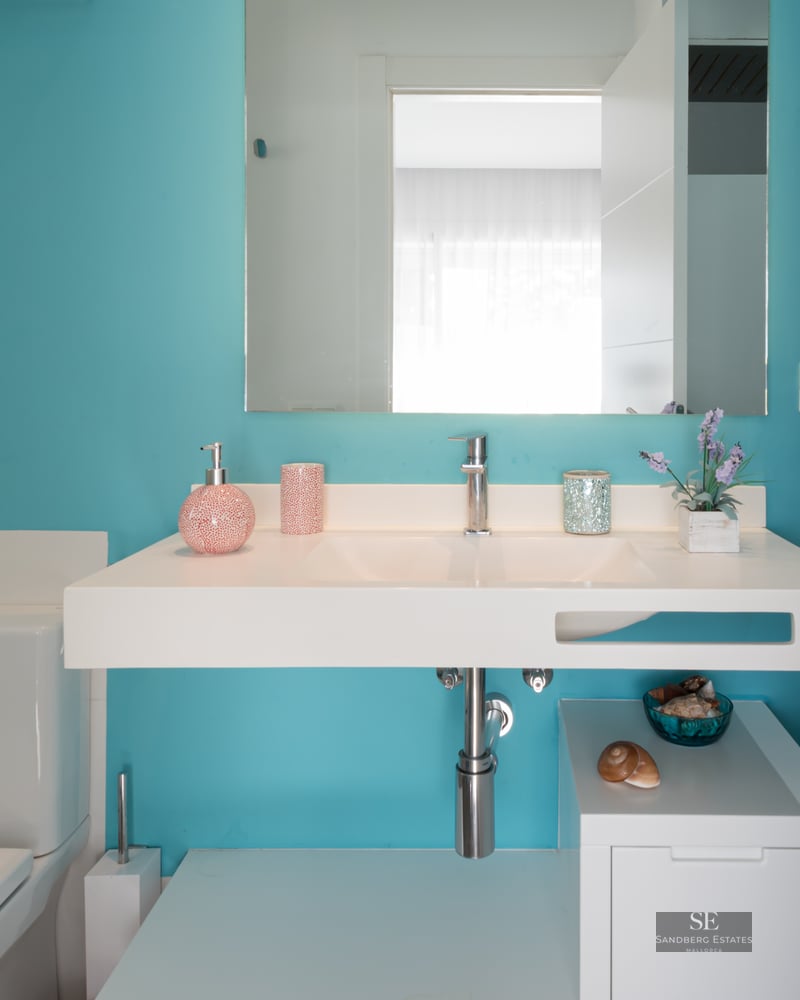 Salle de bain moderne avec mur turquoise, vasque suspendue blanche, grand miroir et toilettes blanches.