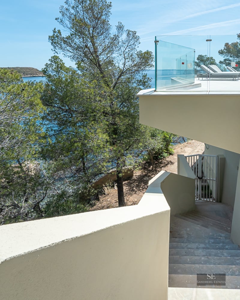 Luxury pool terrace with glass railings and stone stairs overlooking the turquoise Mediterranean Sea and pine trees.