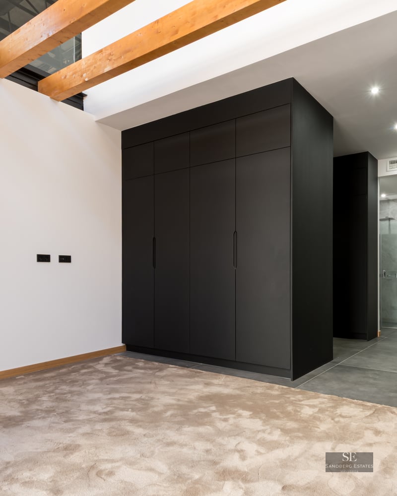 Dressing area featuring large black cabinets, exposed wooden ceiling beams, and plush beige carpeting.