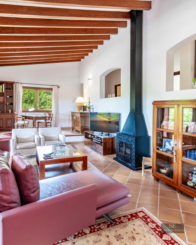 Spacious living room featuring wood ceiling beams, purple sofas, a fireplace, and terracotta flooring.