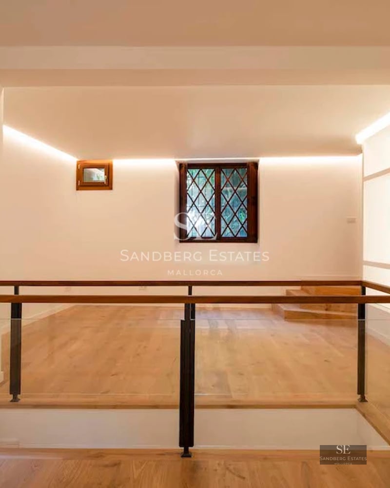 View of a luxurious swimming pool with sun loungers, surrounded by greenery and a modern house with large windows.