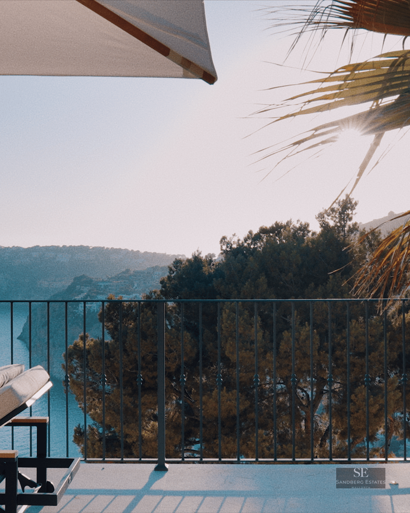 Sun loungers on a modern terrace overlooking a coastal bay and cliffs under a clear blue sky.