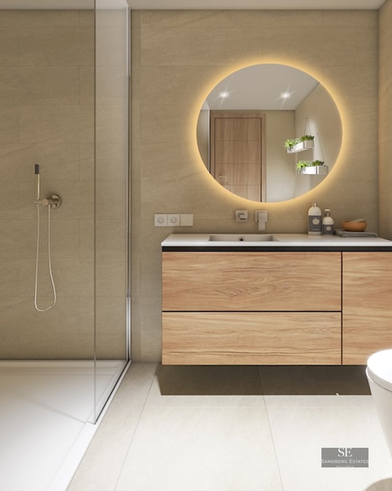 Modern bathroom with walk-in glass shower, wood vanity, backlit round mirror, and wall-mounted plants.