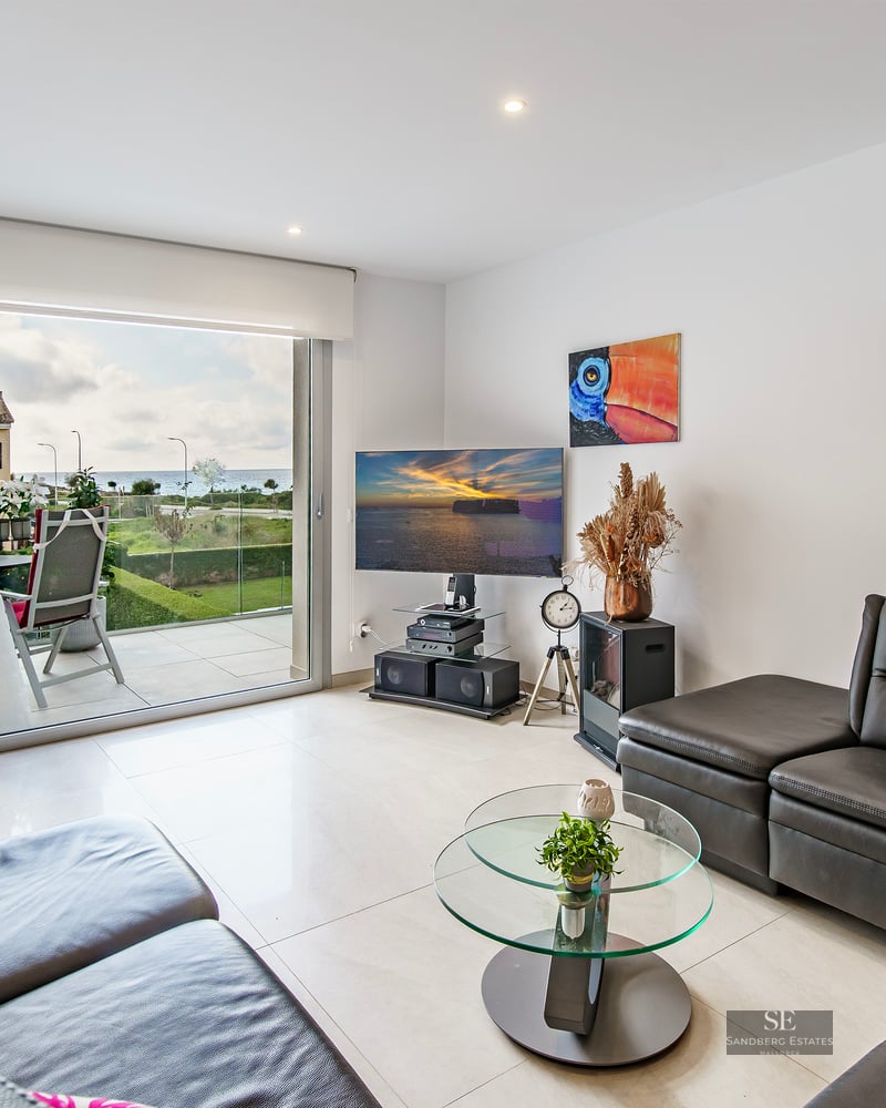 Modern living room with black leather sofas, glass coffee table, and large sliding doors opening to a terrace with sea views.