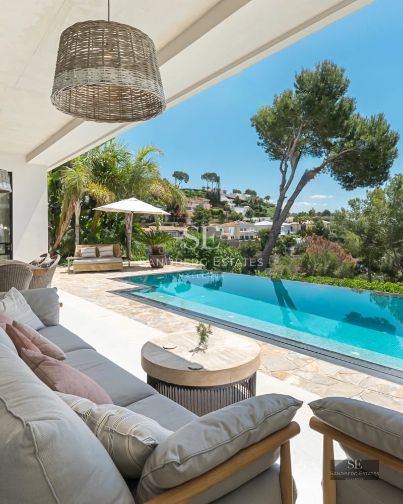 Spacious living room with floor-to-ceiling windows, modern design, gray sofas, glass coffee table, and pool view.