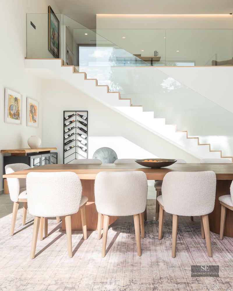 Salle à manger minimaliste avec table en bois, chaises blanches en bouclé et escalier en verre moderne.