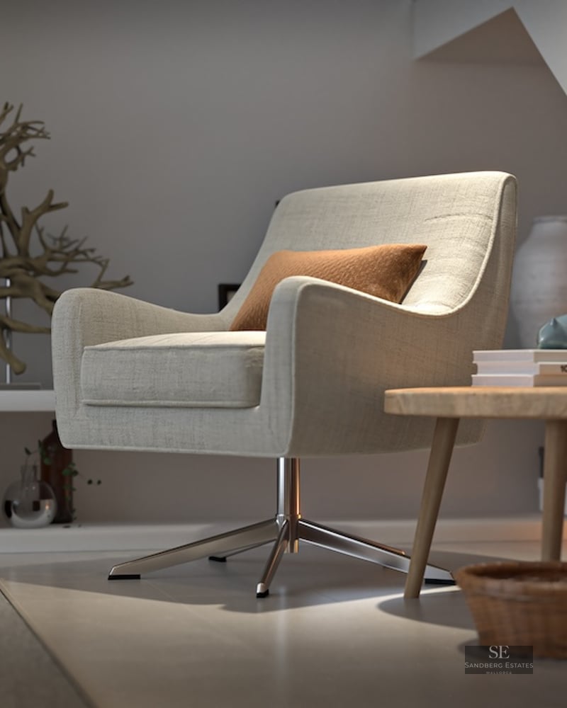A beige swivel armchair in a minimalist interior nook under stairs with a wood table and decorative art pieces.
