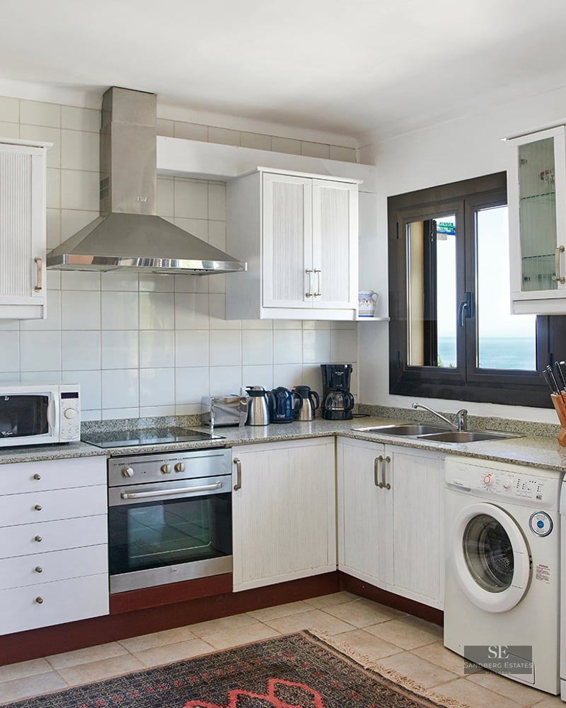 White kitchen with granite countertops, stainless steel appliances, and a window overlooking the ocean.