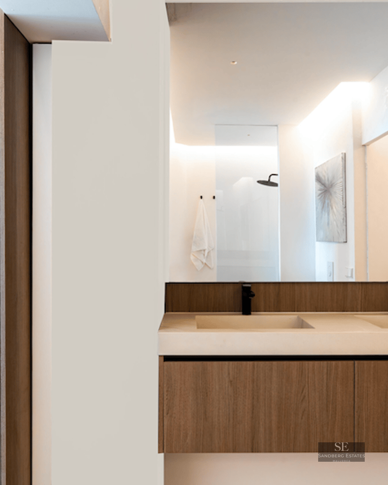 Floating wood bathroom vanity with two sinks and matte black faucets beneath a large frameless mirror.