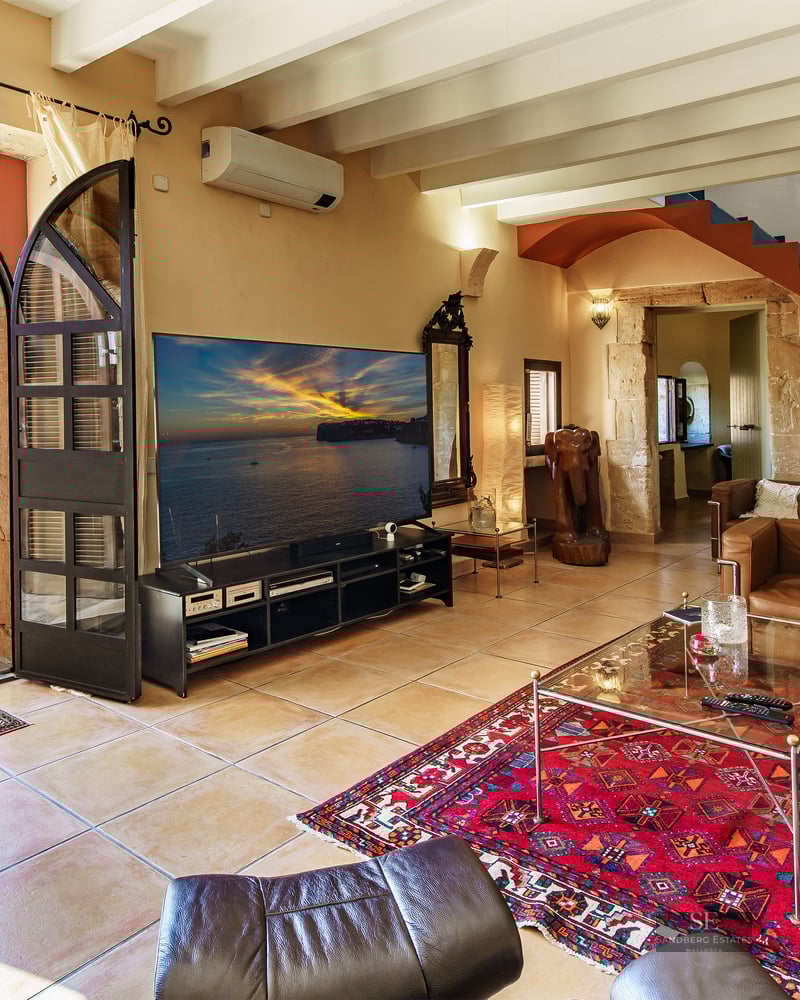 Living room with leather sofas, exposed beams, and a large arch opening to a sunny garden with umbrellas.