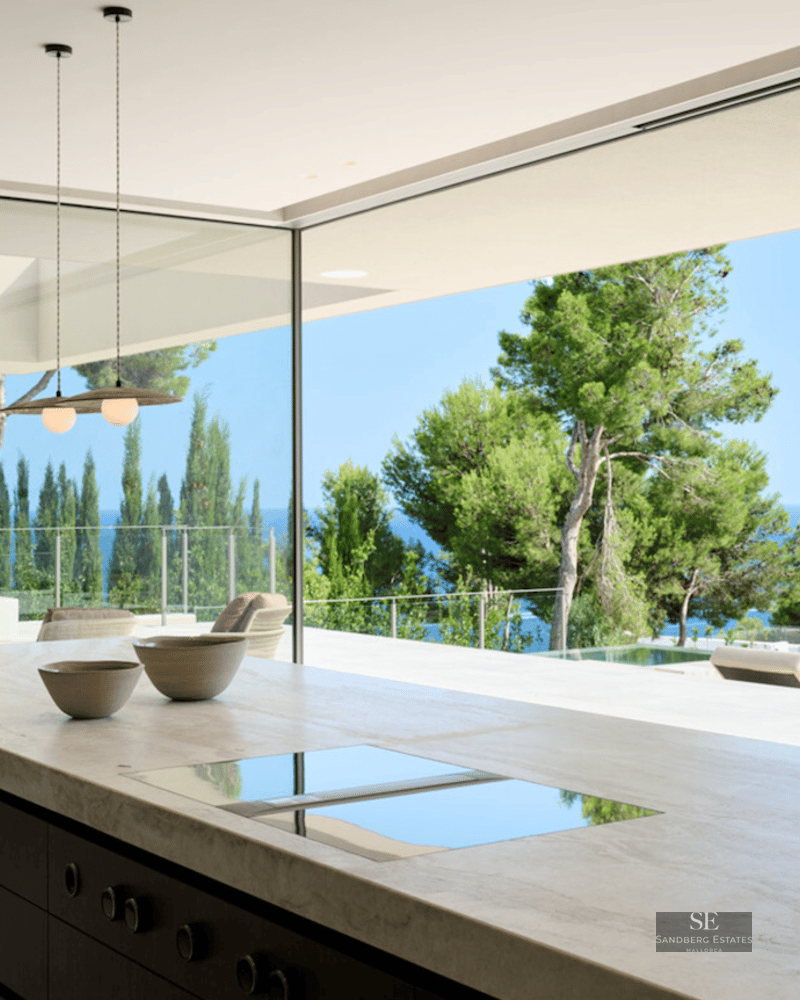 Luxury marble kitchen island facing a large open glass wall with views of a pool and the blue Mediterranean sea.