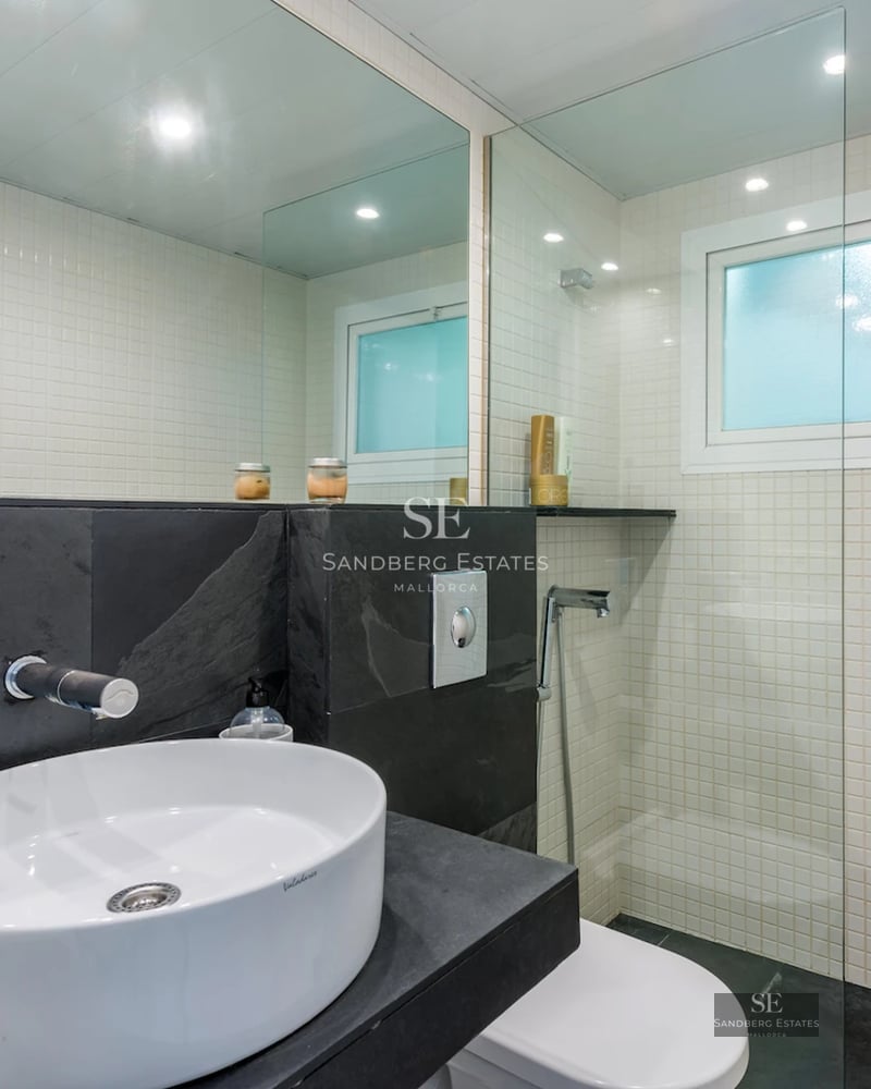 Exterior view of a modern villa with an infinity pool, wooden deck, and large windows. Lush garden with palm trees.