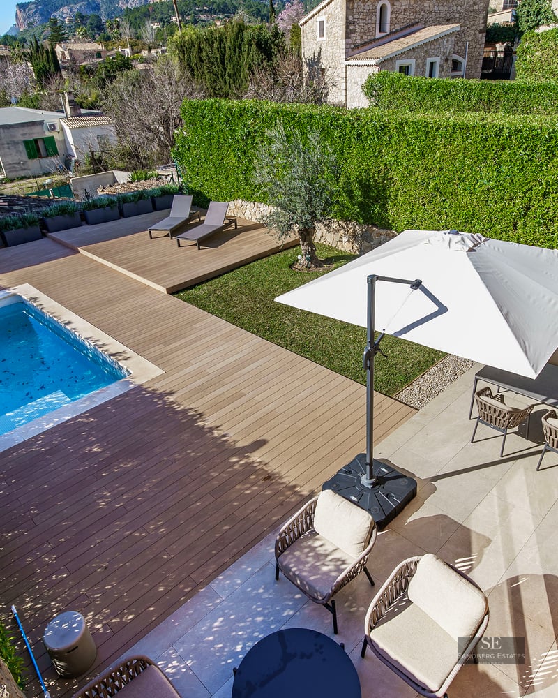 Overhead view of a rectangular swimming pool, wooden deck, lawn, and outdoor dining area surrounded by privacy hedges.