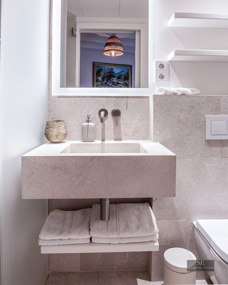 Salle de bain minimaliste avec murs en pierre, lavabo intégré, toilettes suspendues et douche à main chromée.