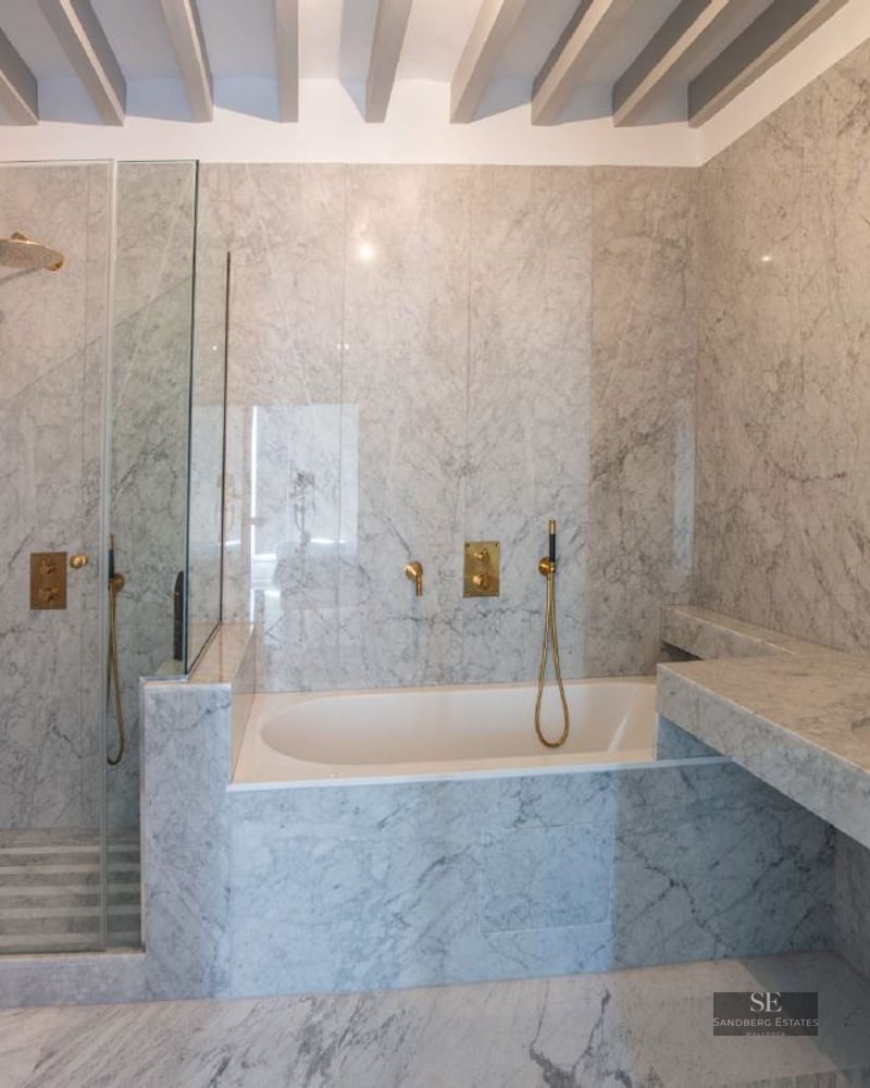 A high-end bathroom featuring marble walls and floors, a glass walk-in shower, a built-in tub, and brass faucets.