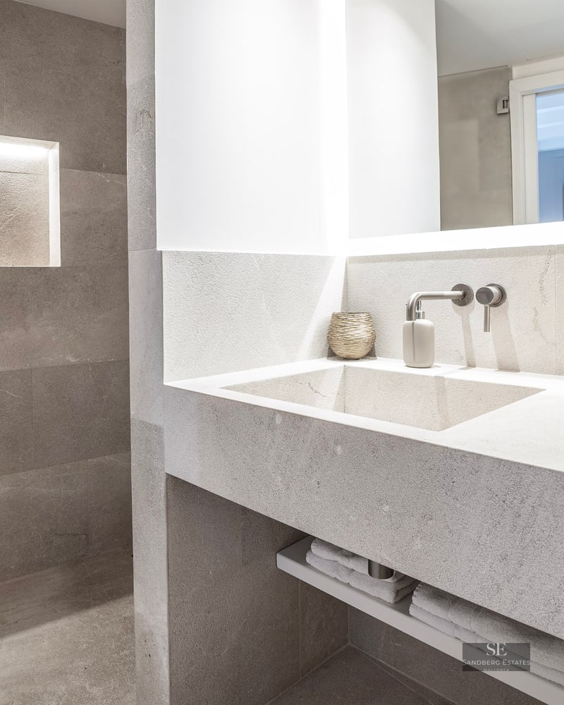 Salle de bain moderne en pierre avec vasque intégrée, robinet mural et niche murale éclairée.