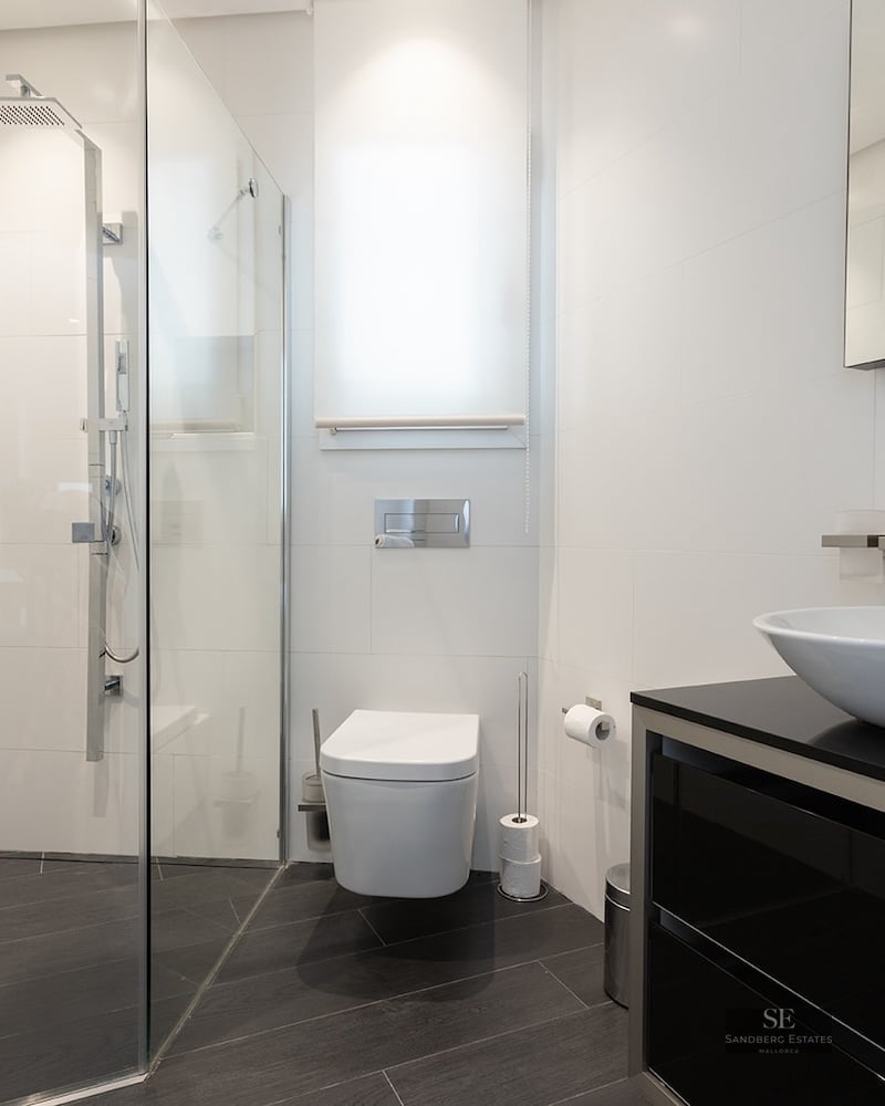 Contemporary bathroom featuring white tiles, walk-in glass shower, wall-mounted toilet, and vessel sink on black vanity.