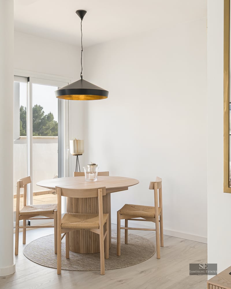 Bright dining area featuring a round wooden table, wicker chairs, black pendant lamp, and terrace access.