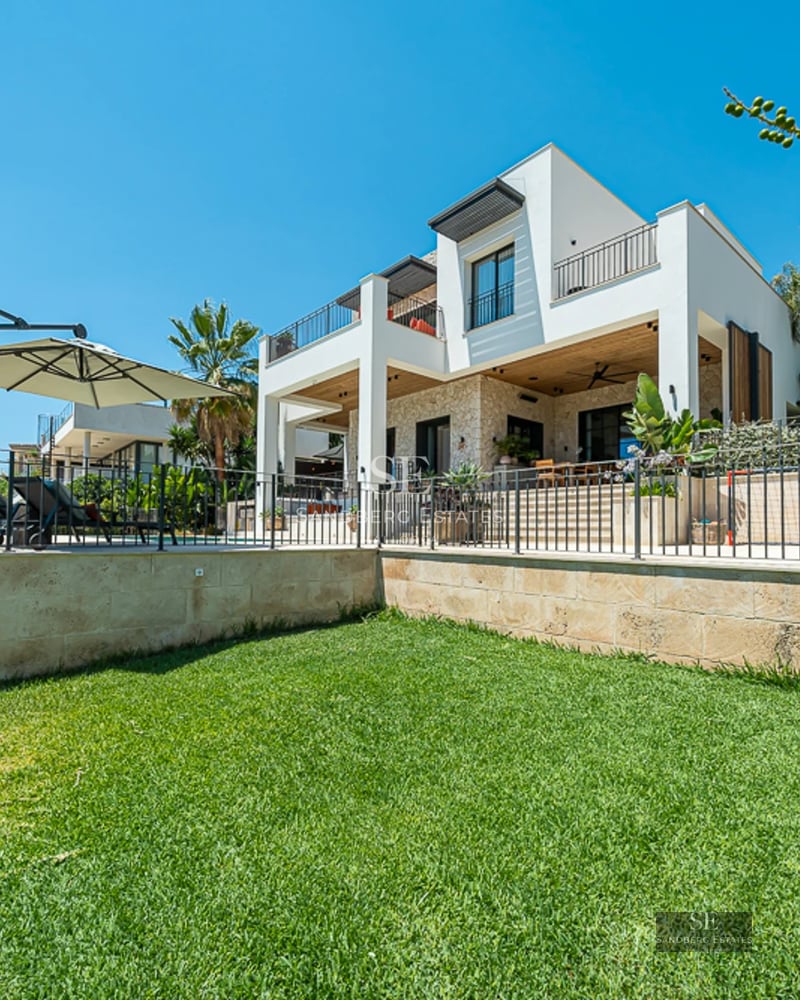Vue extérieure d'une villa moderne avec piscine à débordement, jardins luxuriants et vastes terrasses. Design minimaliste et élégant.