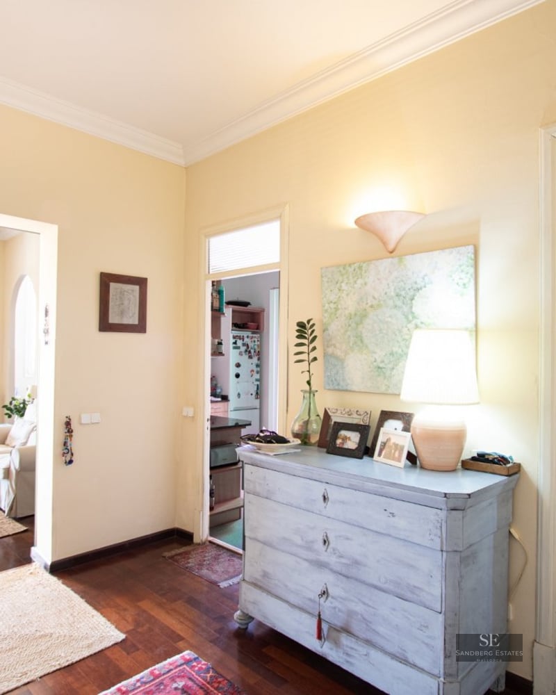 Central hallway with dark wood floors connecting a living room, kitchen, and office in a bright apartment.