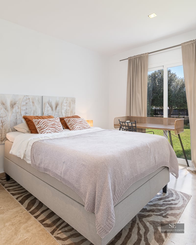 Modern bedroom with marble floors, a double bed, and a large glass door opening to a green garden.