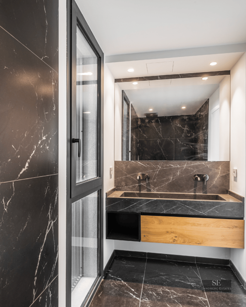 Modern bathroom with black marble walls and floor, an integrated stone sink, and a large mirror.