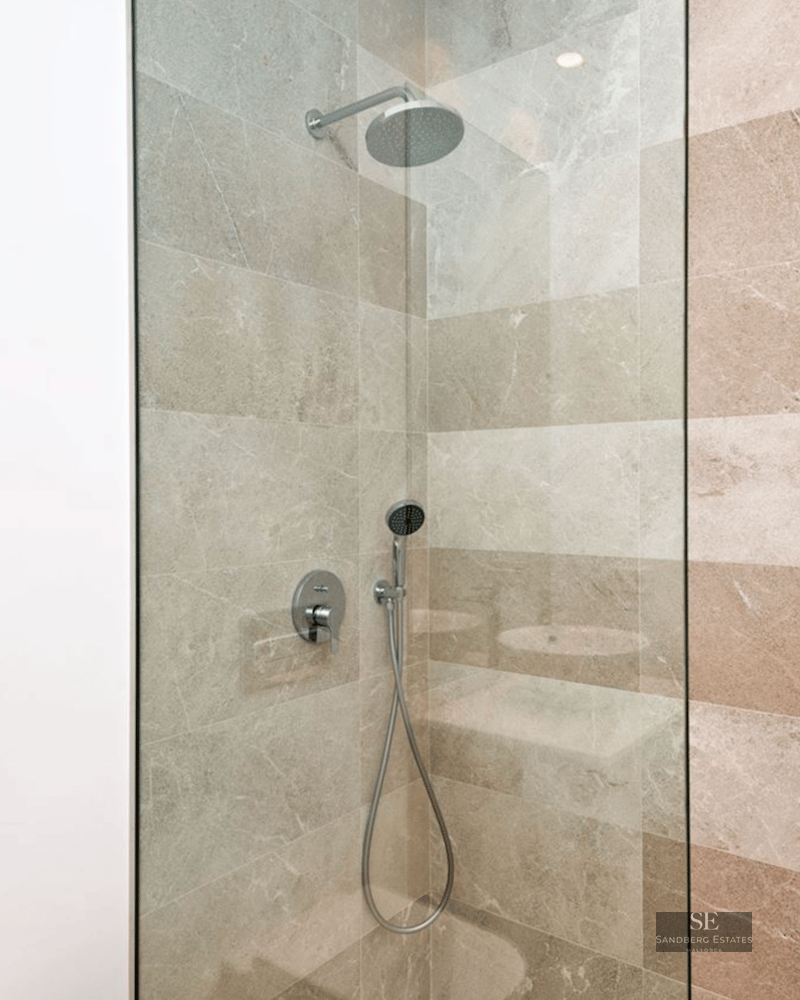 Walk-in shower with rain head, glass screen, and beige stone wall tiles.
