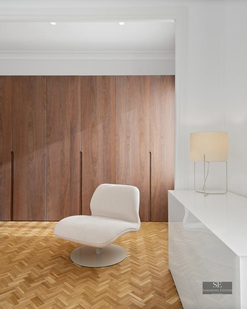 Minimalist dressing area with floor-to-ceiling wood wardrobes, herringbone parquet, and a white designer chair.