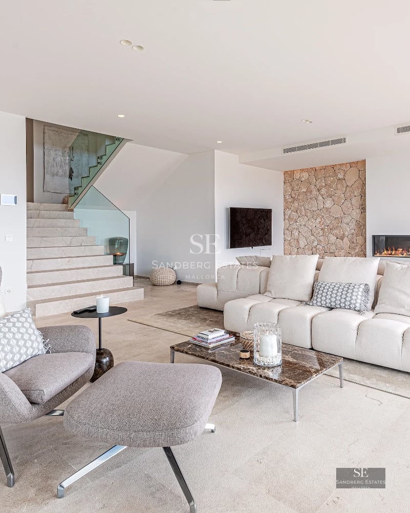View of an infinity pool with loungers and a lush garden, in front of a modern house with large windows.
