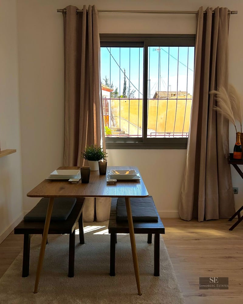 Wooden dining table with benches, neutral curtains, and pampas grass decor by a window.