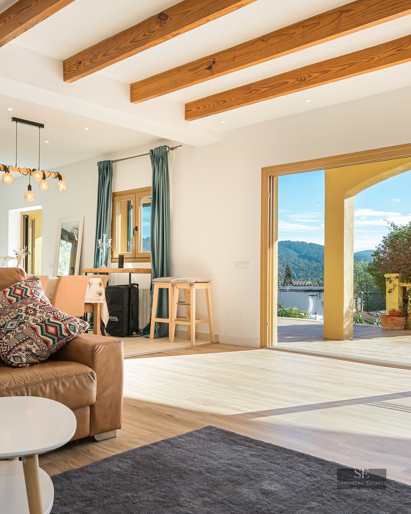 Living room with brown leather sofa, exposed wood beams, and large sliding doors opening to a terrace with mountain views.