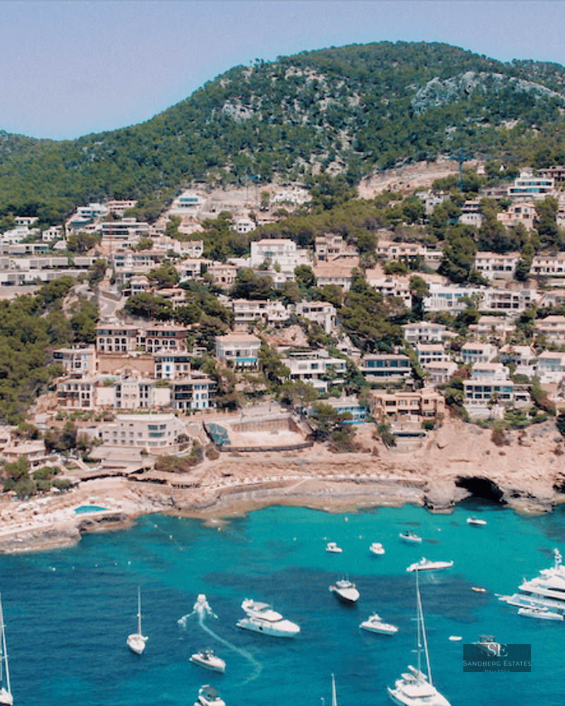 High-angle view of white houses on a green hillside overlooking a bay with many yachts and turquoise water.