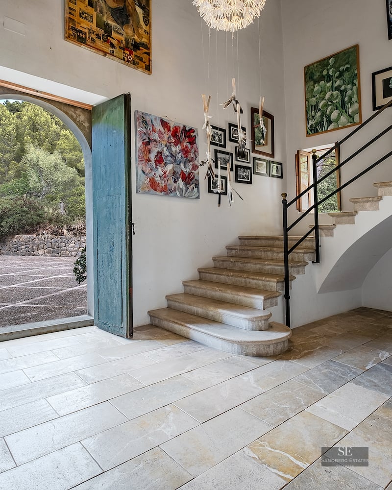 Grand entrance hall with stone floors, high ceilings, a stone staircase, and large green arched doors open to the outside.