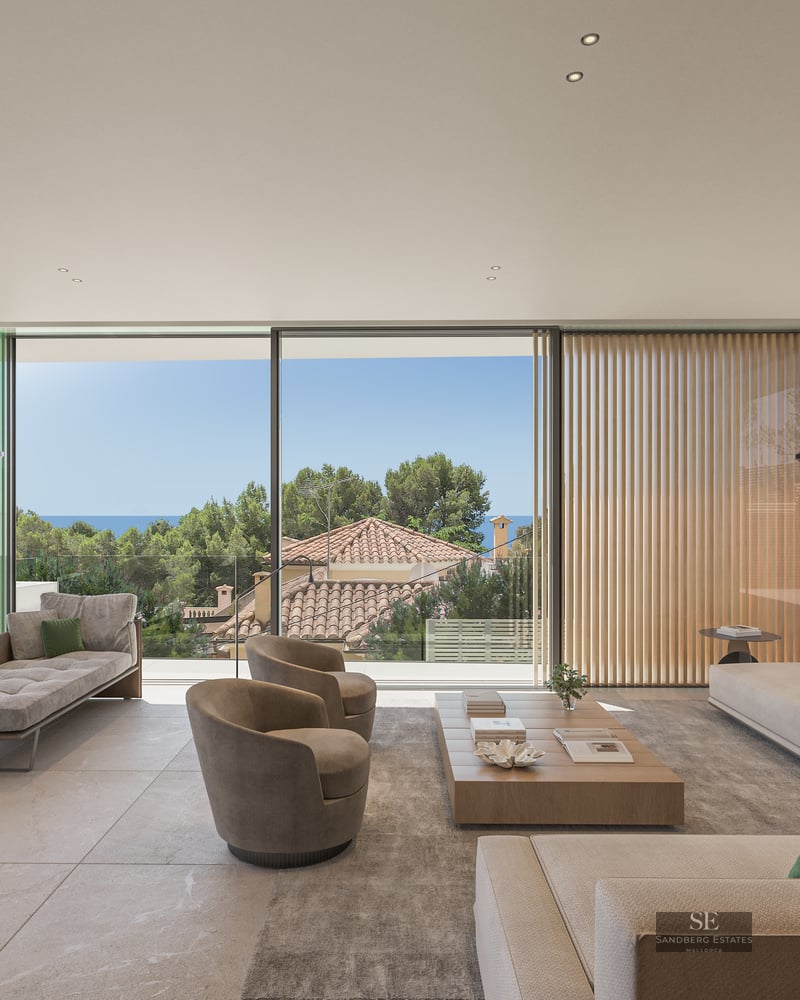 Modern living room with floor-to-ceiling glass walls, beige sofas, wood table, and views of trees and the sea.