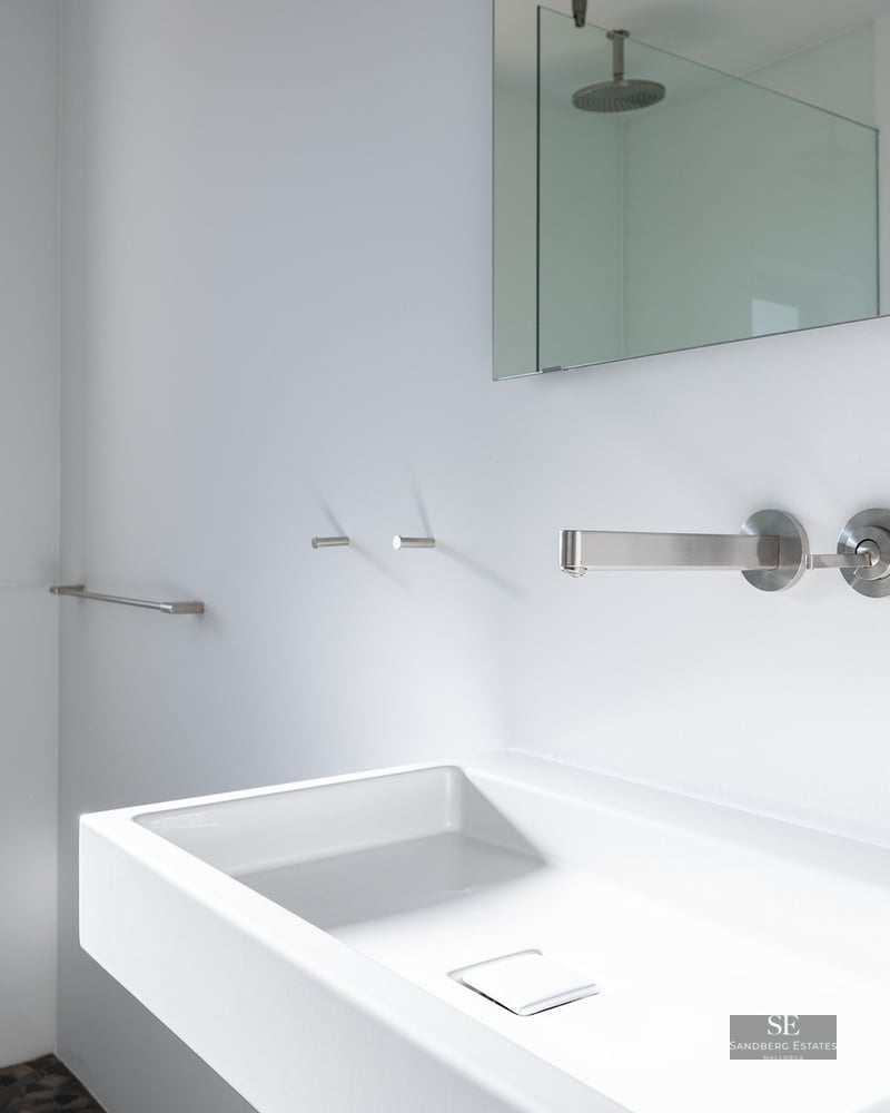 White rectangular sink with wall-mounted chrome faucet in a bright, modern bathroom.