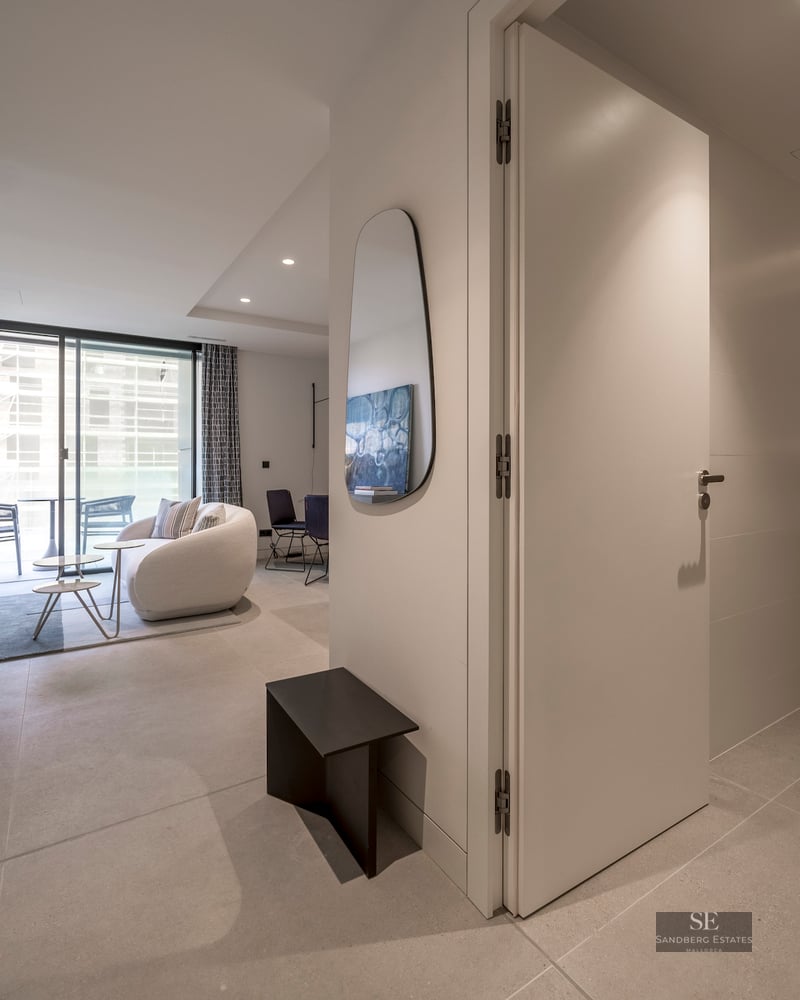 Modern hallway leading to a bright living room with a curved sofa and a sleek bathroom on the right.