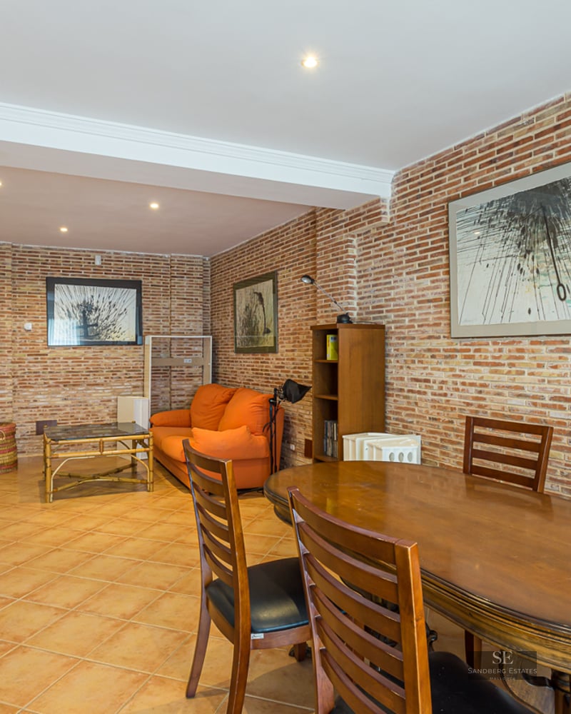 Interior view showing a wooden dining table and an orange sofa against an exposed brick wall.