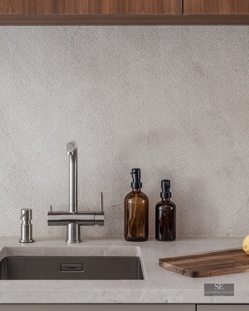 Close-up of a kitchen sink with a stainless steel faucet, stone countertop, and wooden cutting board.
