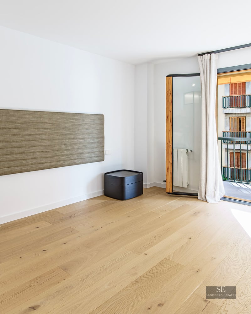Chambre moderne avec parquet en bois clair, tête de lit murale texturée et balcon baigné de lumière naturelle.