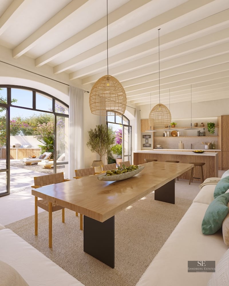 Spacious dining area with a long wooden table, wicker lamps, and large arched windows leading to a sunny terrace.