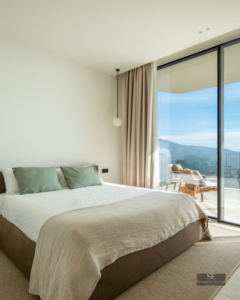 Modern bedroom with floor-to-ceiling windows leading to a terrace overlooking mountains.