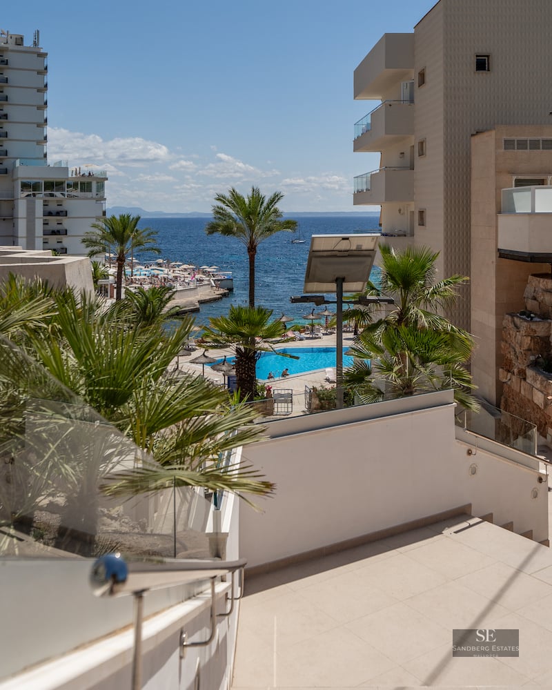 Outdoor stairs with glass railings looking out over a resort pool and the blue Mediterranean Sea.