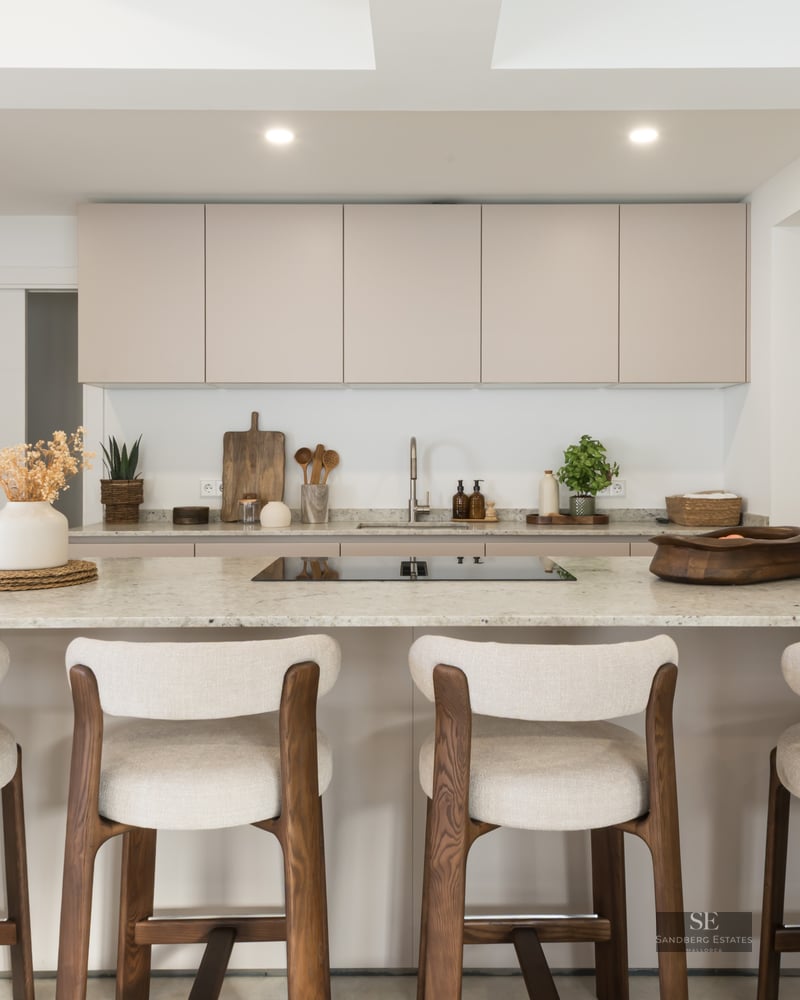 Modern kitchen with beige cabinets, a large stone island, and four wood and fabric bar stools.