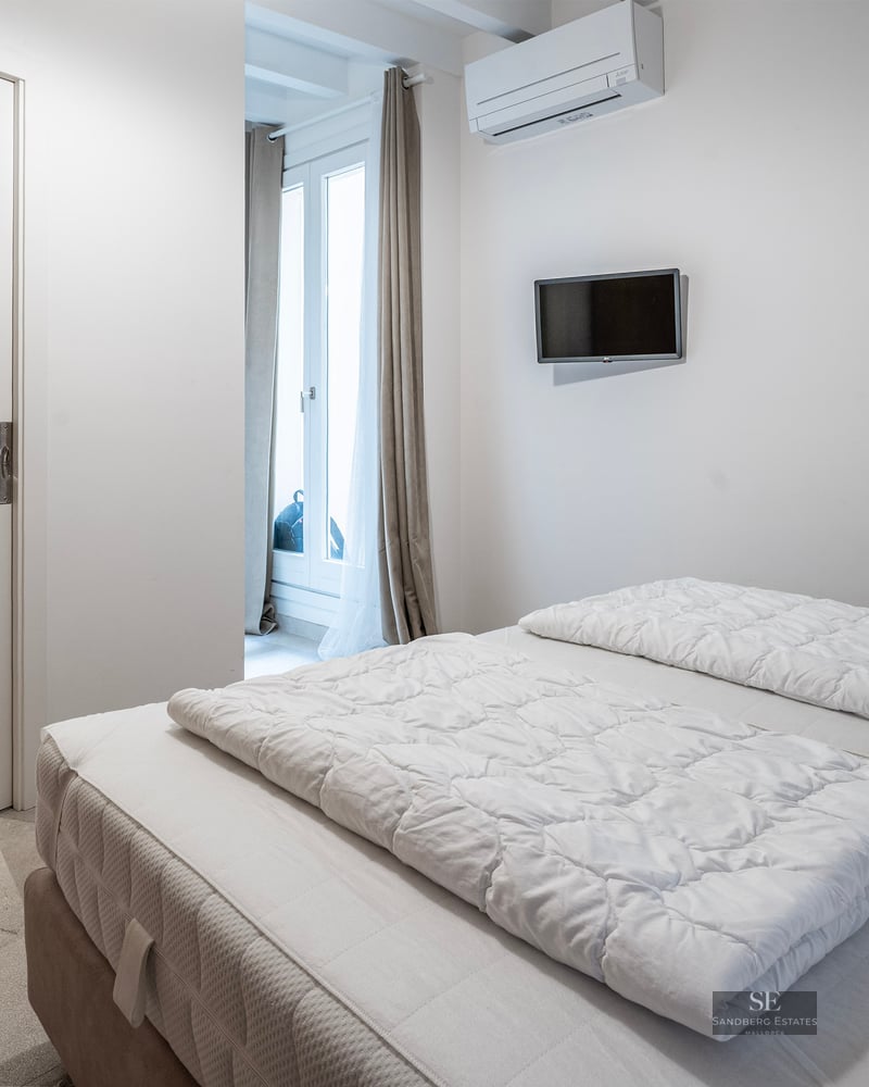 Bright modern bedroom with white bedding and open door to a stone-tiled ensuite bathroom.