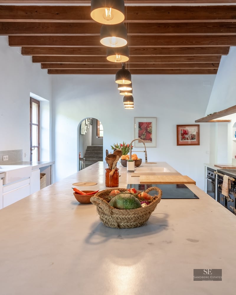 Bright kitchen with wood-beamed ceiling, long stone island, and a vibrant red retro refrigerator.